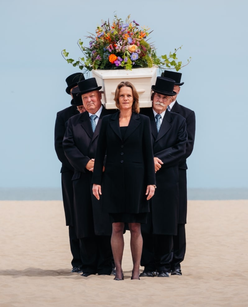begrafenis strand Katwijk Noordwijk Wassenaar uitvaartkist met afscheidsbloemen uitvaart wordt begeleidt door uitvaartleider en dragers